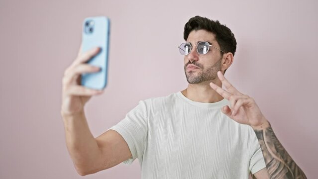 Young hispanic man smiling confident making selfie by the smartphone over isolated pink background