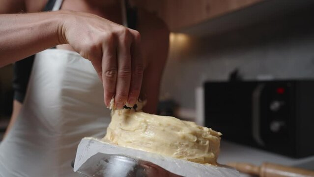 The woman in the white apron sprinkles crumbs of layered pastry on top of the cream of the Napoleon cake. Slow motion