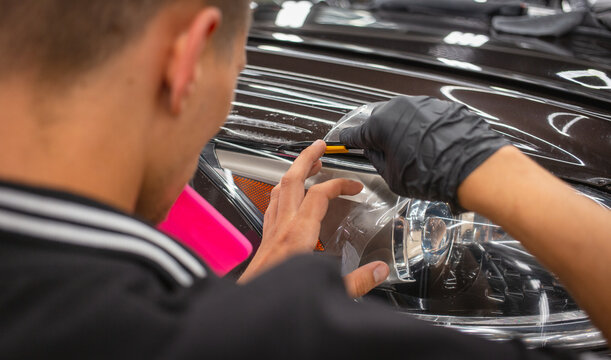 The process of installing a protective polyurethane film for paint on the front headlight of a car.