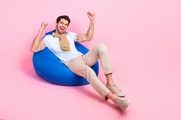 Full body portrait of cheerful satisfied man sit comfy bag raise fists empty space isolated on pink color background