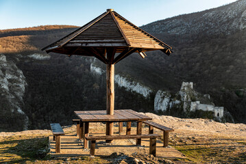 Table in the mountain as resting place with a canopy from the rain and benches, a place to relax in nature. Fortress ruins of Skok Grad in the background, near Soko Banja © Ivan