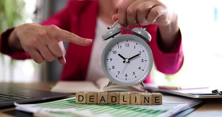 Woman hand holding an alarm clock and deadline text at workplace closeup. Business education concept of time management and working time planning for remote work