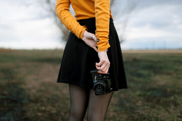 A girl in a black skirt and a yellow jacket stands with her back and holds a camera in her hands from below
