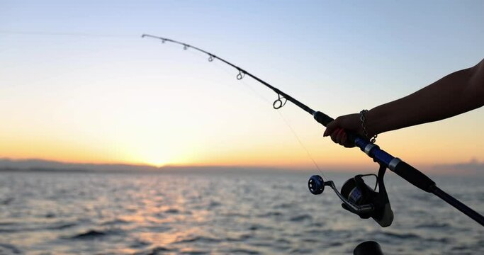 Hands of fisherman holds spinning rod with reel on background of sea. Hobby fishing and tourist