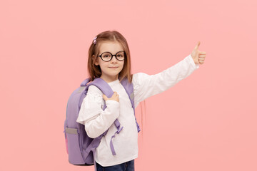 Portrait of a schoolgirl with textbooks and a backpack on a pink background pointing to the right. Back to school