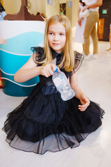 A teenage girl in a black dress tossing a water bottle at a children's party 