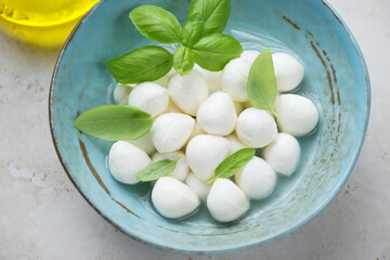 Turquoise bowl with mini mozzarella balls in a brine and fresh green basil, horizontal shot, middle close-up, selective focus