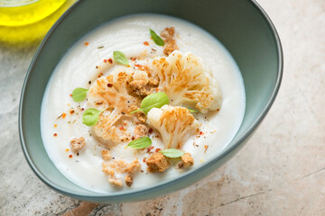 Cauliflower cream-soup served with roasted florets and croutons in a green bowl, middle close-up, horizontal shot, selective focus