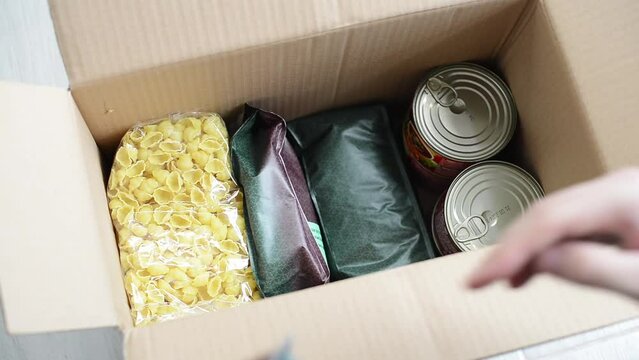 A man collects a box of food to donate to the poor during a pandemic or war. Various products in a box: cereals, rapeseed oil, sunflower oil, canned food. Collection and delivery of food boxes.