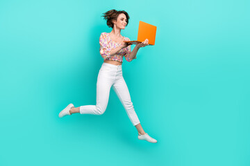 Full size profile portrait of lovely carefree girl jumping run empty space hold netbook isolated on turquoise color background