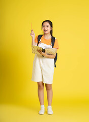 portrait of beautiful asian schoolgirl wearing a backpack on a yellow background.