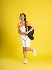 Fototapeta na wymiar portrait of beautiful asian schoolgirl wearing a backpack on a yellow background.