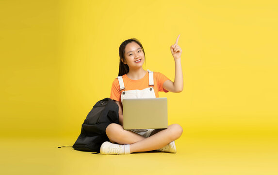 beautiful asian schoolgirl using laptop and  sitting on a yellow background