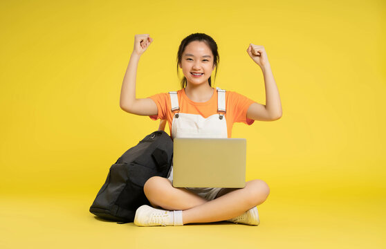 beautiful asian schoolgirl using laptop and  sitting on a yellow background