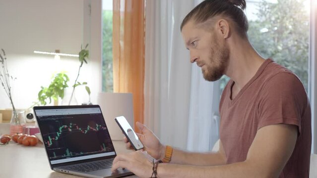Happy man day trading at home on his laptop at the desk while cheering.