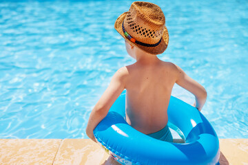 cute kid boy preschooler child on poolside with inflatable ring tube around waist back view summer time vacation swimming in pool sunny day