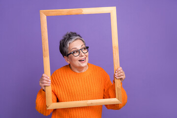 Photo of funny old woman memories portrait frame wooden borders posing model excited look empty space isolated on violet color background