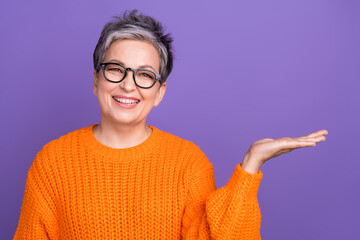 Photo portrait of marketing promoter advertiser pensioner woman holding arm empty space presentation isolated on violet color background - obrazy, fototapety, plakaty