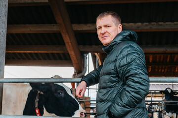 Man Farmer near his cows. Portrait of a young farm owner standing in a long cowshed near the corral...