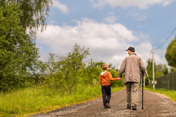grandfather and grandson are walking down road and having conversation on sunny summer day. Copy...