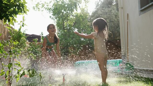 Two Little Child Girls in a Bathing Suits has Fun and Plays with a Watering Hose