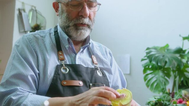 Senior food blogger cutting artichoke, showing its heart on camera and explaining how to cook it during online culinary masterclass in the kitchen
