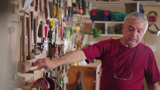 Senior man organizing tools hanging on wall at workshop carpentry shop