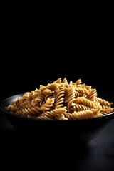Raw pasta fusilli in a bowl on black background