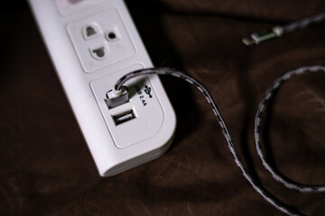 White power socket with black USB charging cable isolated on brown background