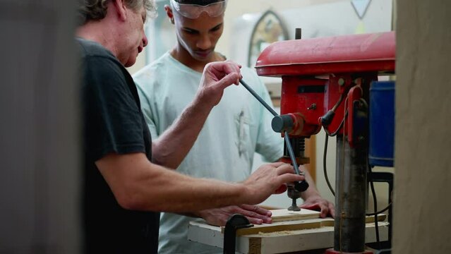 Senior staff guiding carpentry apprentice to use machine at workshop. Candid scene of people working in industrial job, diverse workers