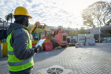 rear view of young black male construction worker supervising construction materials ra