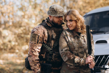 A female US soldier hugs her husband, holding rifles.