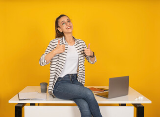 Business woman sit at office desk show thumbs up like gesture with two hands. Young successful...