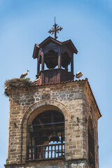 Storks standing on nest atop church bell tower against blue sky