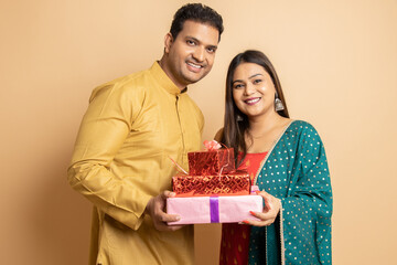 Happy young indian couple wearing traditional cloths holding red gift boxes celebrating of diwali...
