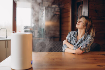 A modern humidifier while relaxing, a happy European young woman, a girl enjoying the aromatherapy steam scent from an essential oil diffuser.