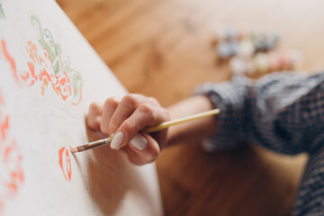 A girl in a checkered shirt is painting with a brush on a canvas, drawing by numbers. Selective...