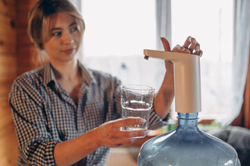 automatic water pump. A smiling woman pours water into a glass. Blurred background. Space for text.