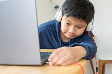 Asian cute kid boy reaches out to plug his headphones into his laptop by himself with a face that intends to use the computer to study online at home. link and connect
