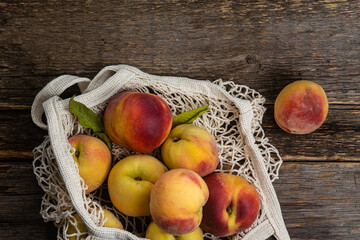 Ripe peaches in eco bag on wooden background