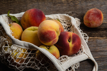 Ripe peaches in eco bag on wooden background