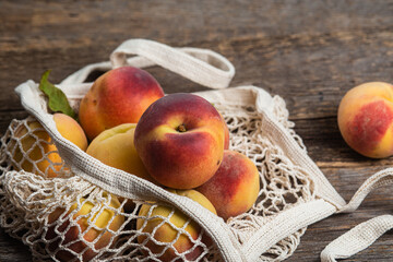 Ripe peaches in eco bag on wooden background