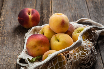 Ripe peaches in eco bag on wooden background