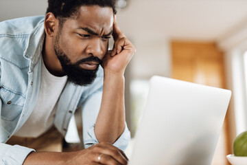 Pensive black entrepreneur brainstorming while working on a computer at home