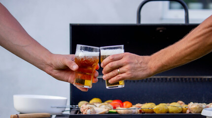 men hold beer in their hands on the background of the grill, vegetables and meat. Selective focus.