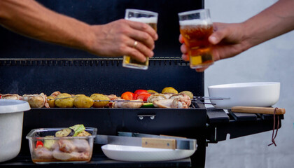 men hold beer in their hands on the background of the grill, vegetables and meat. Selective focus.