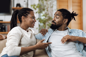 Happy black couple talking while relaxing on sofa at home