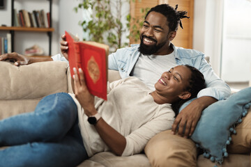 Happy black couple relaxing on sofa at home and reading a book