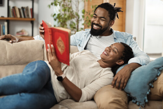 Happy black couple relaxing on sofa at home and reading a book