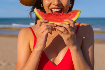 Portrait of a woman eating a watermelon by the beach. Cutout of mouth smiling with red bikini